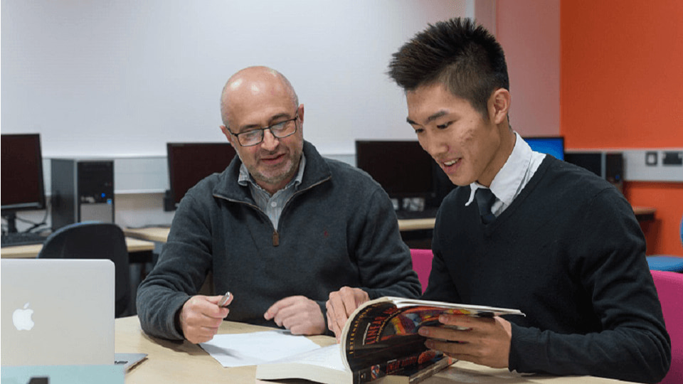 Student and tutor sat at table with an open book